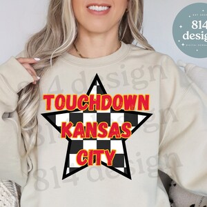 May include: A beige sweatshirt with a black and white checkered star design. The star has the words "TOUCHDOWN KANSAS CITY" in red text.