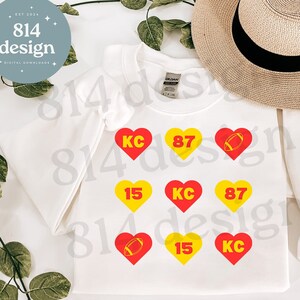 May include: White sweatshirt with red and yellow hearts featuring the numbers 87, 15, and KC. The hearts also have a football graphic and the text "814 design".
