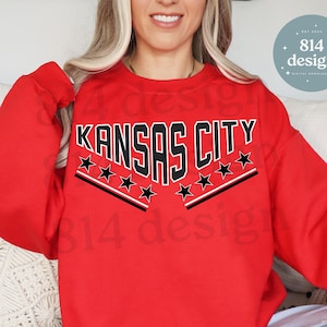 May include: Red sweatshirt with black text that reads "Kansas City" with black stars above and below the text.