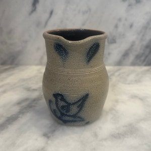 May include: A small, blue and white stoneware pitcher with a bird design and the words "New England Pottery Works, Handcrafted in USA" on the side.