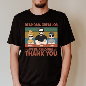 May include: Black t-shirt with a vintage-style graphic that says "Dear Dad, Great Job" with three cartoon figures of a dad and two children. The text below the figures says "We're Awesome Thank You" with the names Olivia, John, and Liam under the figures.