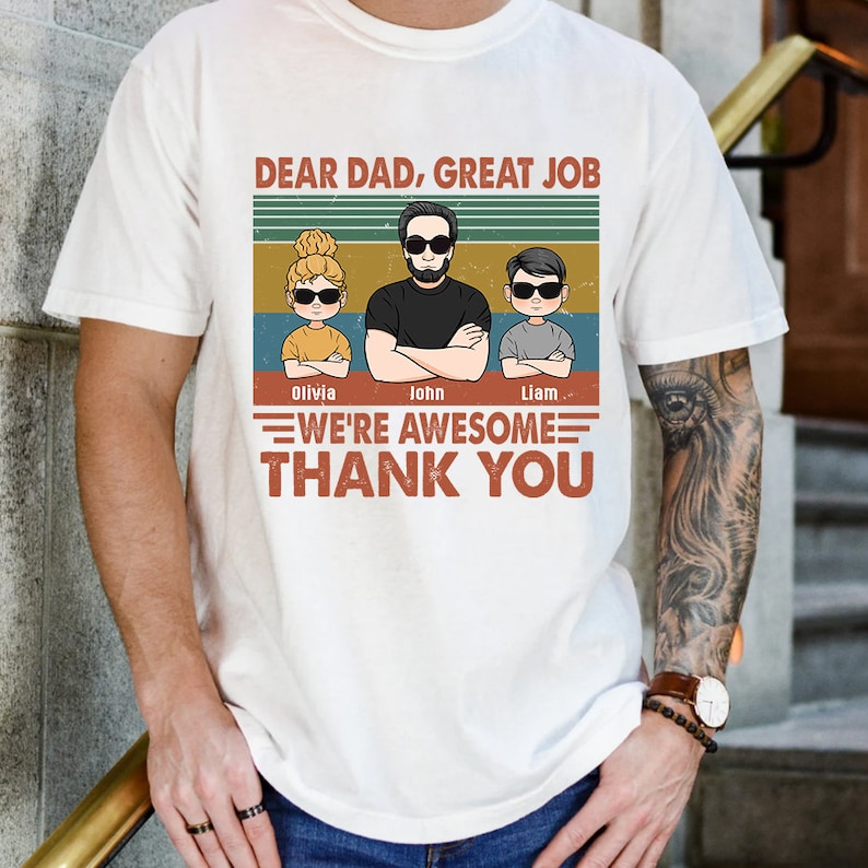 May include: A white t-shirt with a vintage-style graphic featuring a dad and three children. The text reads "Dear Dad, Great Job We're Awesome Thank You". The children's names are Olivia, John, and Liam.