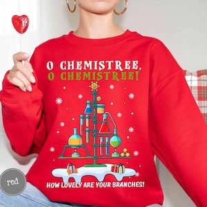 May include: A red sweatshirt with a science-themed Christmas tree design. The tree is made of lab equipment, with the text "O Chemistree, O Chemistree! How lovely are your branches!" printed on the front.