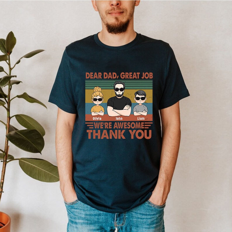 May include: A navy blue t-shirt with a vintage-style graphic that says "Dear Dad, Great Job" with a cartoon image of a dad and two children. The children's names are Olivia, John, and Liam. The graphic also says "We're Awesome" and "Thank You".