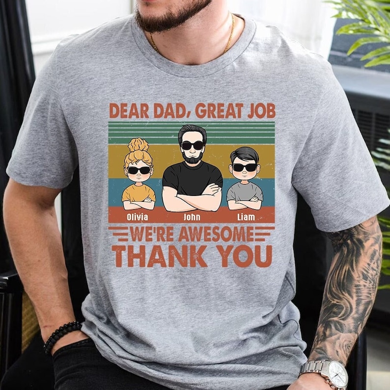 May include: A gray t-shirt with a vintage-style design featuring a dad and two children. The text reads "Dear Dad, Great Job We're Awesome Thank You". The children's names are Olivia, John, and Liam.