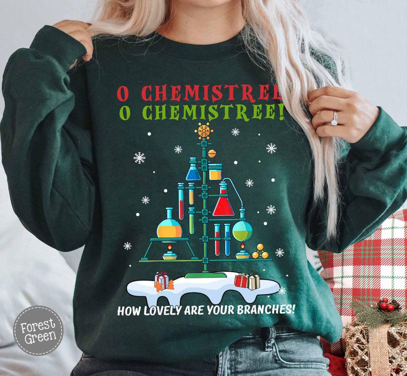 May include: Forest green sweatshirt with a Christmas tree design made of laboratory equipment. The text "O Chemistree! How lovely are your branches!" is printed on the front, along with snowflakes and gift boxes.