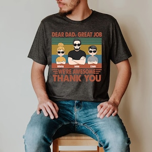 May include: A gray t-shirt with a retro-style design featuring a father and two children. The text reads "Dear Dad, Great Job. We're Awesome. Thank You." The children's names are Olivia, John, and Liam.