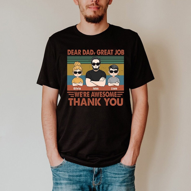 May include: Black t-shirt with a vintage-style graphic that says "Dear Dad, Great Job" with three cartoon figures of a dad and two children. The text below the figures says "We're Awesome Thank You" with the names Olivia, John, and Liam under the figures.
