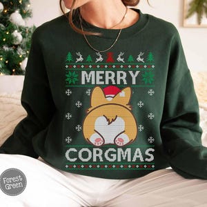 May include: Green Christmas jumper with a white and red pattern. The jumper features a cartoon image of a corgi wearing a Santa hat with the text "Merry Corgmas".