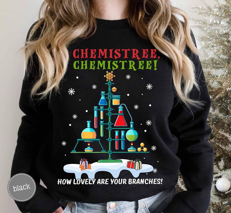 May include: Black sweatshirt with a Christmas tree design made of laboratory glassware. The text "CHEMISTREE, CHEMISTREE! HOW LOVELY ARE YOUR BRANCHES!" is printed in green and white. Snowflakes and gift boxes complete the festive look.