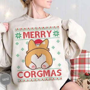 May include: A cream-coloured sweatshirt with a festive Christmas design featuring a cartoon corgi wearing a Santa hat. The text "Merry Corgmas" is printed on the sweatshirt.