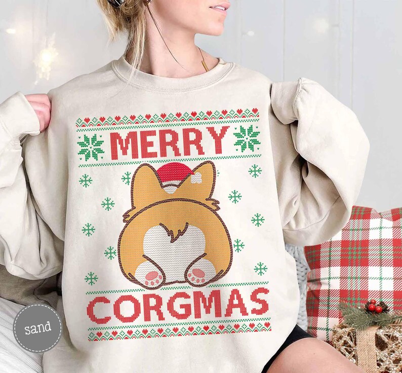 May include: A cream-coloured sweatshirt with a festive Christmas design featuring a cartoon corgi wearing a Santa hat. The text "Merry Corgmas" is printed on the sweatshirt.