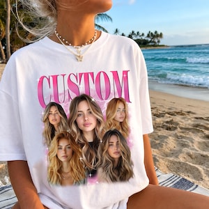 May include: White t-shirt with the word "CUSTOM" in pink, featuring a photo collage of a woman with long, wavy hair. The shirt is worn on a beach with ocean and palm trees in the background.
