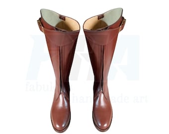 May include: A pair of brown leather riding boots with a front zipper and buckle detail. The boots have a tall shaft and a smooth, polished finish. The interior lining is a lighter shade of brown.