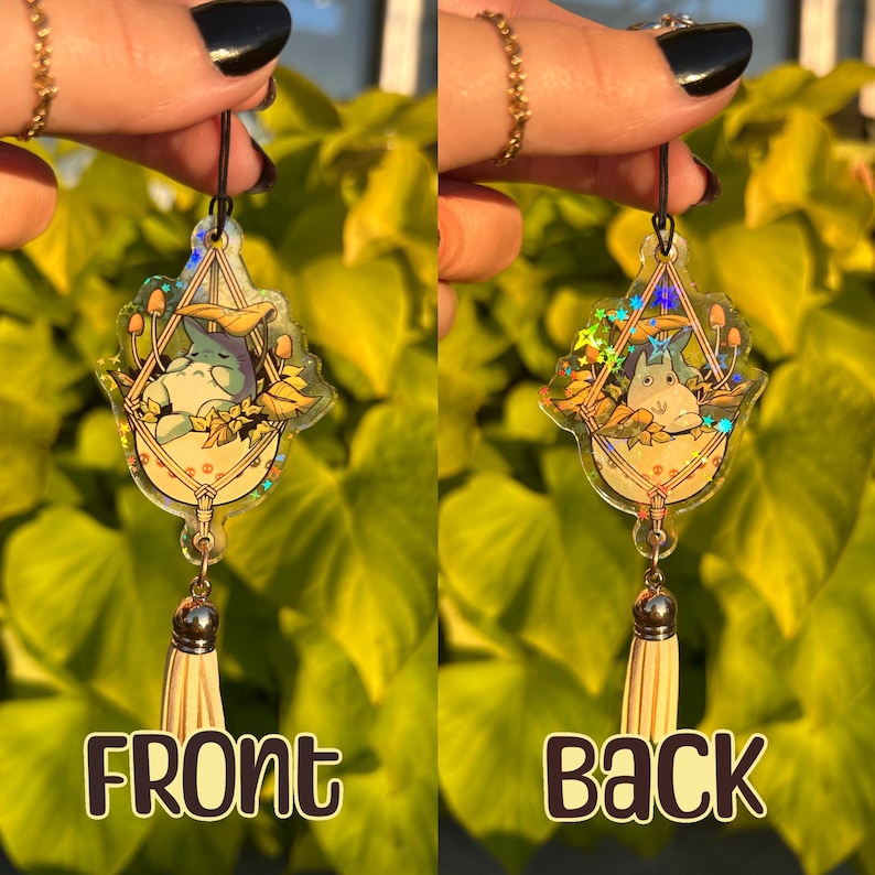 May include: A clear acrylic charm featuring a cartoon character in a hammock with mushrooms and leaves. The charm has a silver-colored tassel and the word "FRONT" is printed on the front. The back of the charm has the word "BACK".