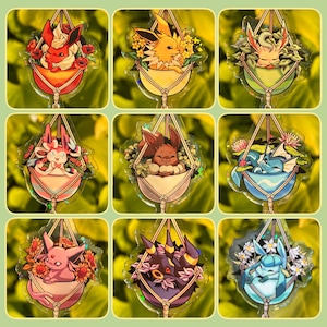 May include: Nine colourful acrylic charms featuring various Pokémon characters nestled in hanging planters filled with flowers. Each charm has a unique design, with vibrant colours and intricate details. The charms are set against a green background.