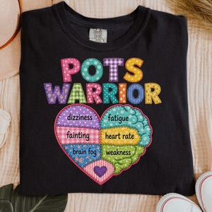 May include: Black t-shirt with the text "POTS WARRIOR" in colorful patchwork letters. Below the text is a heart-shaped graphic divided into sections, each labeled with a symptom: dizziness, fatigue, fainting, heart rate, brain fog, and weakness.
