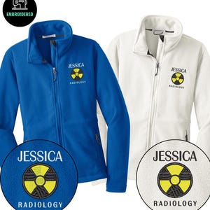 May include: Two fleece jackets, one blue and one white, with a zip-up front and a high collar. Each jacket has the name "JESSICA" embroidered above a yellow and black radiology symbol. The word "RADIOLOGY" is embroidered below the symbol.