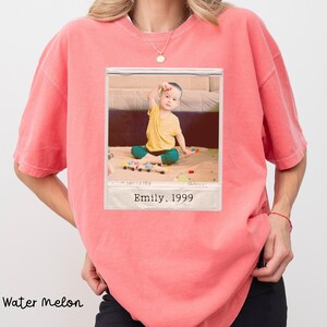 Peut inclure: T-shirt couleur past&egrave;que avec une photo encadr&eacute;e d'un enfant. La photo montre un enfant en chemise jaune et pantalon vert jouant avec des jouets. La photo porte l'inscription "Emily, 1999".