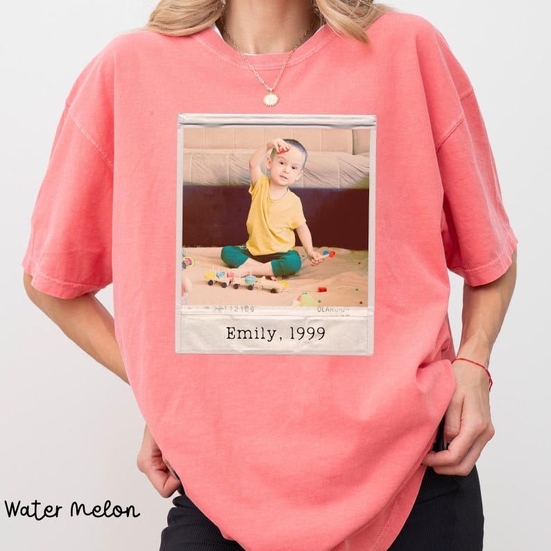 Peut inclure: T-shirt couleur past&egrave;que avec une photo encadr&eacute;e d'un enfant. La photo montre un enfant en chemise jaune et pantalon vert jouant avec des jouets. La photo porte l'inscription "Emily, 1999".