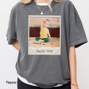 Peut inclure: Un t-shirt gris fonc&eacute; surdimensionn&eacute; avec une image imprim&eacute;e d'un enfant en chemise jaune et pantalon vert. L'image est encadr&eacute;e comme un polaroid avec le texte "Emily, 1999". Le t-shirt est de style d&eacute;contract&eacute;.