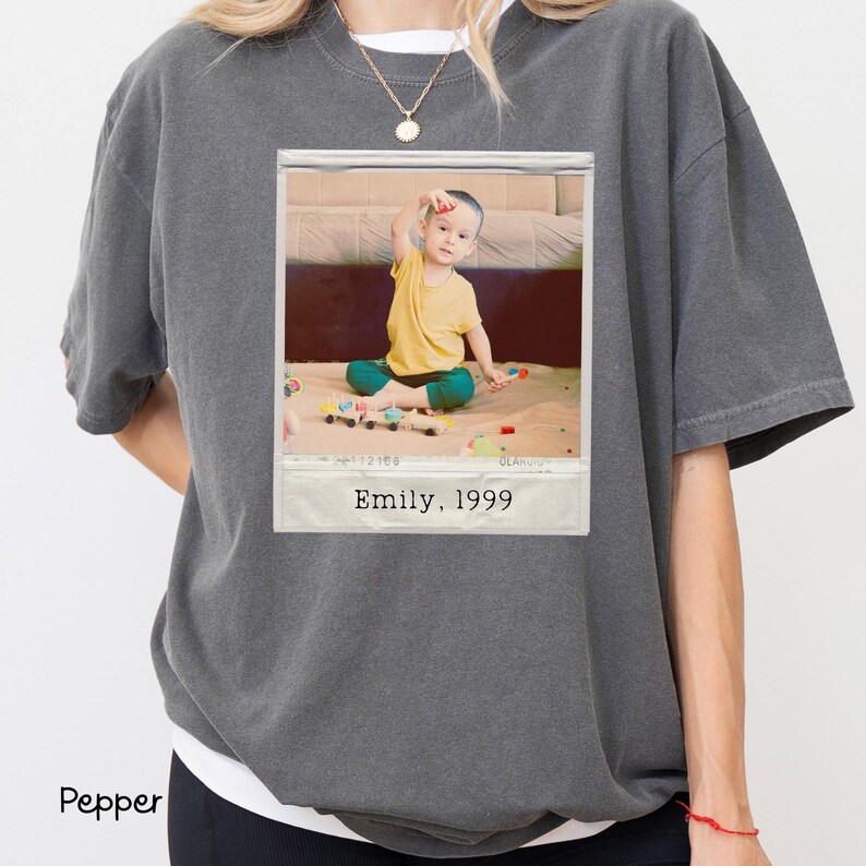 Peut inclure: Un t-shirt gris fonc&eacute; surdimensionn&eacute; avec une image imprim&eacute;e d'un enfant en chemise jaune et pantalon vert. L'image est encadr&eacute;e comme un polaroid avec le texte "Emily, 1999". Le t-shirt est de style d&eacute;contract&eacute;.