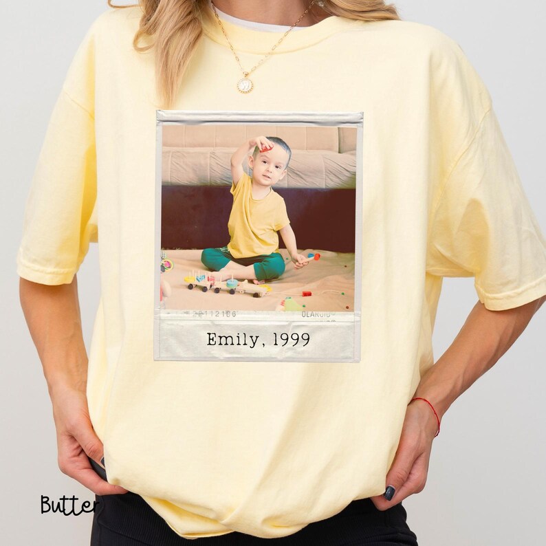 Peut inclure: T-shirt jaune clair avec une photo encadr&eacute;e d'un enfant. La photo montre un enfant en haut jaune et pantalon turquoise jouant avec des jouets. Le texte "Emily, 1999" est imprim&eacute; au bas de la photo.