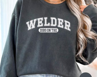 May include: A dark grey sweatshirt with the text "Welder Dibs on the" in white. The text is in a collegiate font.