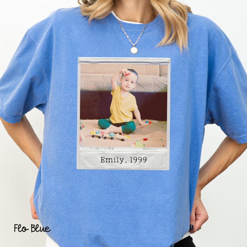 Peut inclure: Sweat-shirt bleu Flo avec un imprim&eacute; photo encadr&eacute;. La photo montre un enfant en chemise jaune et pantalon vert jouant avec des jouets. Le texte "Emily, 1999" est visible.