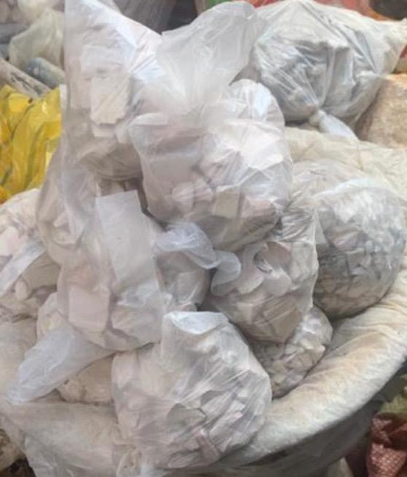 May include: A collection of multiple translucent white plastic bags filled with small, irregular, off-white stone or mineral fragments. The bags are bunched together, showing a textured, crinkled surface and containing numerous solid pieces.