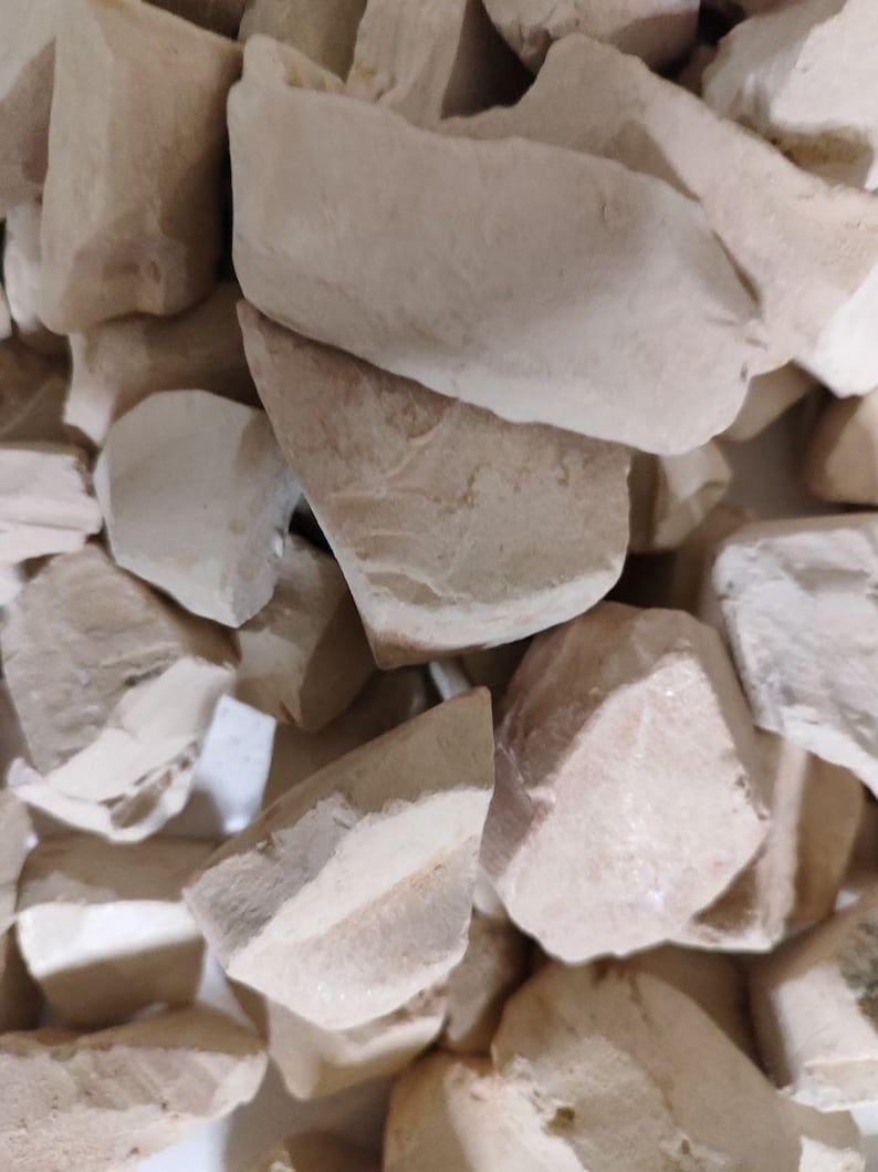 May include: A collection of irregular, chunky pieces of off-white, matte-textured clay or chalk. The fragments vary in size and shape, displaying rough, fractured edges and a solid, opaque appearance throughout the entire cluster of material.