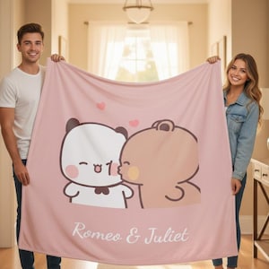 May include: A light pink blanket featuring a cartoon illustration of two bears kissing, with hearts above them. The blanket has the words "Romeo & Juliet" in white script at the bottom.