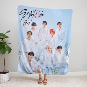 Puede incluir: Una manta azul y blanca con un grupo de ocho hombres vestidos de blanco. La manta tiene el texto "Stray Kids" y "Lisa" impreso en ella.