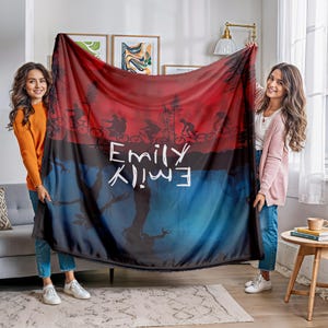 K&ouml;nnte beinhalten: Eine gro&szlig;e, rechteckige Decke mit einem roten und blauen Farbverlauf, die Silhouetten von Radfahrern und B&auml;umen zeigt. Der Name "Emily" ist wei&szlig; gedruckt, mit einer gespiegelten Version darunter. Die Decke wird von zwei Personen gehalten.
