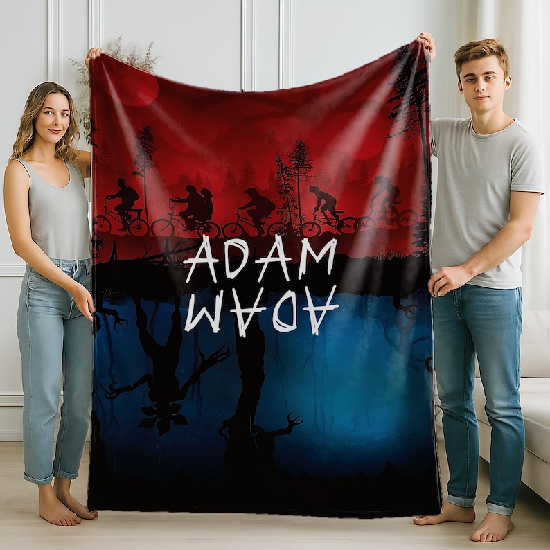 K&ouml;nnte beinhalten: Eine rot-blaue Decke mit einer Silhouette von Radfahrern vor rotem Himmel. Die Decke tr&auml;gt den wei&szlig;en Schriftzug "ADAM", darunter der gleiche Text gespiegelt. Die untere H&auml;lfte der Decke ist blau mit einer dunklen Baumsilhouette.
