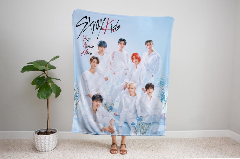 Puede incluir: Una manta de tiro azul y blanca con un grupo de ocho hombres vestidos de blanco. La manta presenta el texto "Stray Kids" y "Your Name Here".