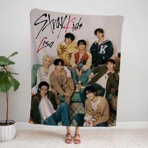 Puede incluir: Un grupo de ocho j&oacute;venes est&aacute;n representados en una manta. La manta es de color crema con un dise&ntilde;o rosa y negro. El texto "Stray Kids" y "Lisa" est&aacute; escrito en la manta. Los j&oacute;venes visten ropa informal y est&aacute;n sentados y de pie en una variedad de poses.