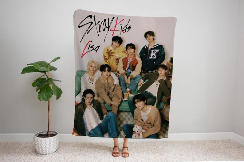 Puede incluir: Un grupo de ocho j&oacute;venes est&aacute;n representados en una manta. La manta es de color crema con un dise&ntilde;o rosa y negro. El texto "Stray Kids" y "Lisa" est&aacute; escrito en la manta. Los j&oacute;venes visten ropa informal y est&aacute;n sentados y de pie en una variedad de poses.