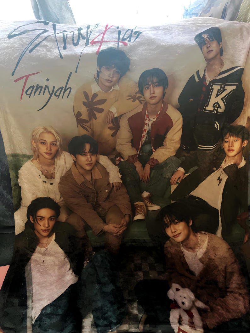 Puede incluir: Una manta blanca con un grupo de siete j&oacute;venes vestidos con ropa informal. La manta tiene el texto "Stray Kids" y "Taniyah" impreso en ella.