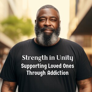 May include: A man wearing a black t-shirt with the text "Strength in Unity Supporting Loved Ones Through Addiction" printed in white.
