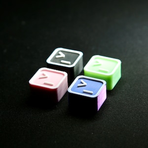 May include: Four small, square-shaped, colorful blocks with a white command prompt symbol on each. The blocks are black, pink, green, and purple.