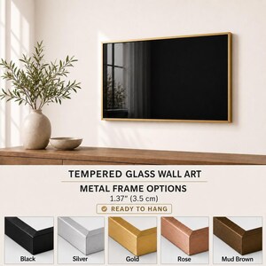 a wall art display with a black framed picture hanging on a wall. The wall art is mounted on a wooden shelf, and there is a vase with a plant on the shelf. The image also includes a selection of metal frame options available for hanging the wall art, along with a description of the frame options.