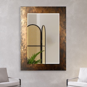 Pode incluir: Um espelho retangular grande com uma moldura de bronze desgastada. O espelho reflete uma sala com uma tela tecida e uma planta em vaso.