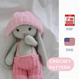 Puede incluir: Patrón de crochet para un conejito gris que lleva un gorro rosa y un mono. El patrón está disponible en inglés y es una descarga PDF.