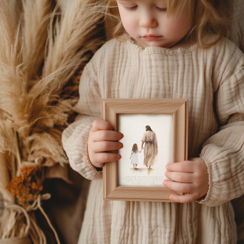 May include: A child holds a framed print of a watercolor painting depicting a man and a young girl walking hand-in-hand. The text below the image reads "For I am the Lord your God, who takes hold of your right hand and says to you, Do not fear; I will help you."