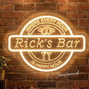 Puede incluir: Un letrero de neón para "Rick's Bar" brilla intensamente contra una pared de ladrillos. El letrero dice "Where Every Hour Is Happy Hour" y presenta un logotipo con dos copas. Estantes debajo exhiben varias botellas de licor, creando un ambiente cálido.