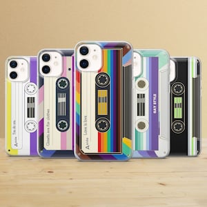 Könnte beinhalten: Fünf Handyhüllen mit Kassettenband-Designs. Die Hüllen weisen verschiedene Farben auf, darunter Regenbogen, Lila und Schwarz, mit Texten wie "Love is love" und "Gay Style". Die Hüllen befinden sich auf einer Holzoberfläche.