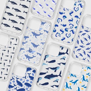 May include: Clear phone cases with various blue whale and fish patterns. Designs include whales, fish, and stars on a white background. The cases are made of clear plastic and are designed to fit a smartphone.