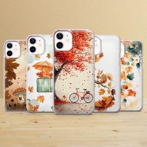 Op de afbeelding: Vijf verschillende telefoonhoesjes met herfstthema's. De hoesjes bevatten afbeeldingen van herfstbladeren, een eekhoorn, een fiets en een koffer. De hoesjes zijn allemaal transparant en hebben een witte achtergrond.