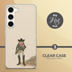 K&ouml;nnte beinhalten: Eine transparente Handyh&uuml;lle mit einem vollfl&auml;chigen Druck einer Frosch, der einen Cowboyhut und ein Bandana tr&auml;gt. Der Frosch steht auf einem braunen und wei&szlig;en Hintergrund mit goldenen Sternen. Der Text "Big Hug Hub" ist in einem Kreis auf der H&uuml;lle gedruckt.